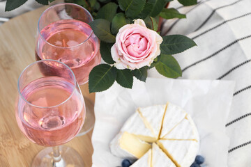 Glasses of delicious rose wine, flower and food on white picnic blanket
