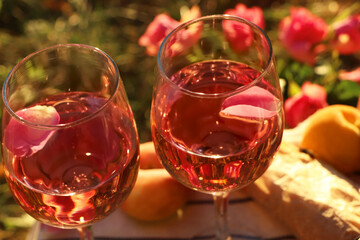Glasses of delicious rose wine with petals outside, closeup