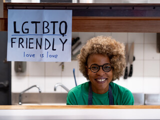 Smiling african american woman with afro hair looking at camera in a restaurant holding a sign:...