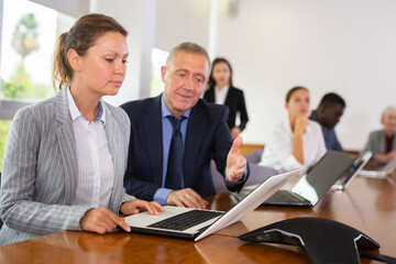 Obraz premium Woman secretary using laptop and discussing job with her employer, middle aged man, during meeting in conference room.