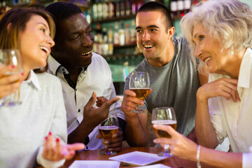 Company of multiracial friends drinking beer and talking with each other during the rest in a pub