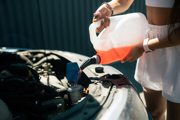 Young woman pouring antifreeze car screen wash liquid into car