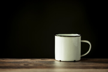a white enameled metal cup of coffee on a wooden table