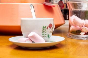 A cup of tea with drawings on the porcelain, a metal spoon inside and accompanying marshmallows