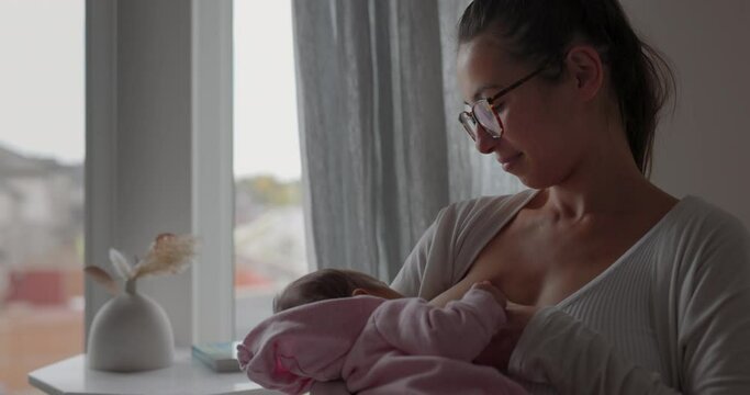 Young mother nurses her newborn baby girl in babys room - medium shot
