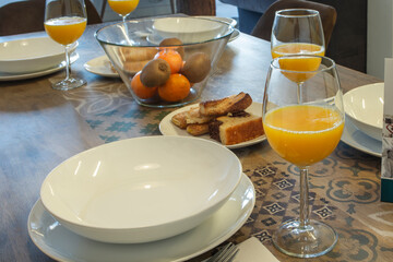 A table full of deep and flat plates together with glasses full of orange juice and recipes with fresh fruits