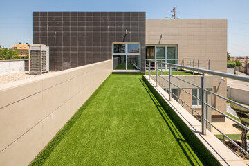 Fototapeta na wymiar Elongated terrace in the shape of an L covered with artificial grass overlooking a summer pool and in front of the facade of the house