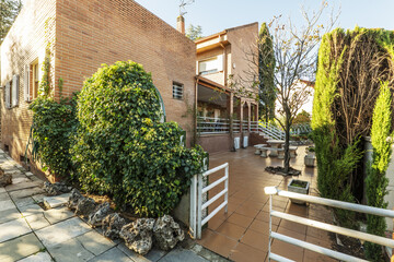 Naklejka premium Terrace with clay tiles, white metal fences, hedges, potted plants and trees in a chalet