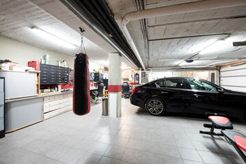 A detached house garage with gray floors, a punching bag and a parked luxury vehicle - obrazy, fototapety, plakaty