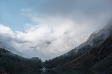 Tranquil scenery with snow mountain range in clouds and alpine lake. Mountain creek flows from...