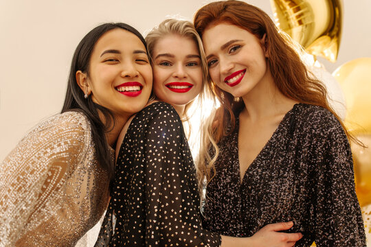Beautiful young interracial girls with red lipstick smiling looking at camera indoors. Blonde, brunette and redhead wear dresses on holiday. Bachelorette party concept