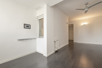 Empty living room of a house with dark laminated flooring, white plain walls and a small built-in wall safe