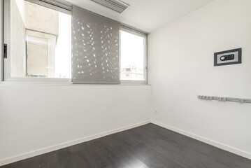 Empty living room of a house with a dark brown laminate floor, a wall-to-wall window and white walls