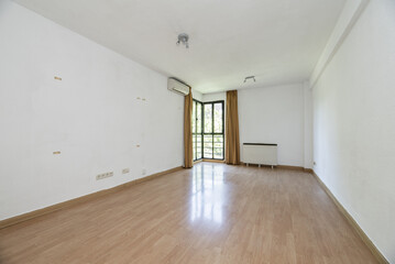 Empty living room of a house with light-colored laminate flooring, a corner with a gabled bay window and an electric heater
