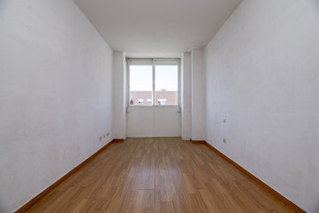 Empty living room of a house with old wood color laminate flooring and walls in need of a fresh coat of paint
