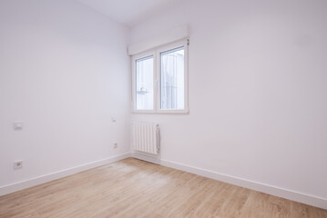 Empty living room of a house with light wood laminate floors, a white aluminum radiator under the window and freshly painted white plain walls