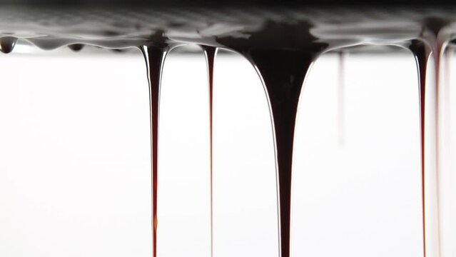 Seamless dripping dark caramel or melted chocolate droplets flowing down liquid sweet sauce on white background. Close-up shot flowing brown orange tasty syrup drip. Confectionery, cooking candies