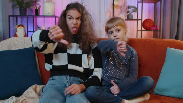 Dislike. Upset teenage child and little sister kid showing thumbs down sign gesture, expressing discontent, disapproval, dissatisfied bad work. Displeased siblings children or friends at home playroom