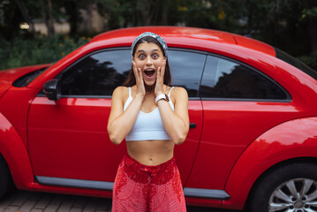 Portrait of pretty Caucasian woman standing against new red car