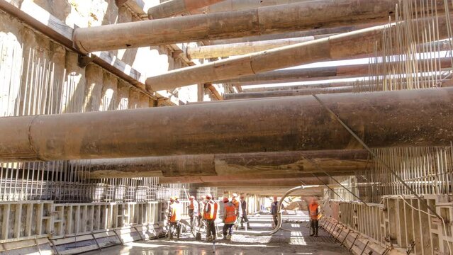 Workers pouring concrete in large huge ditch pit tunnel timelapse. Reinforcing structures from thick iron pipes of beams and structures at the construction site of the underground metro station line.