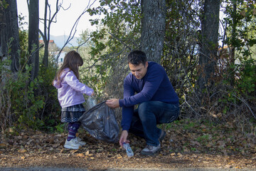 Father and daughter in the woods collecting plastic bottles. Cleaning and recycling of nature. Safeguarding the planet.
