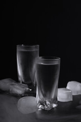 Vodka in shot glasses with ice on table against black background