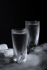 Vodka in shot glasses with ice on table against black background