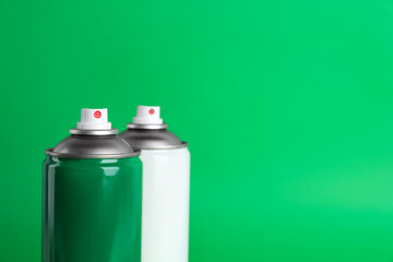 Two cans of spray paints on green background. Space for text