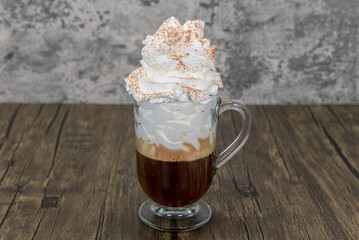 Dark roast strong coffee topped tall with sweet whipped cream in a clear mug as a morning energy boosting drink