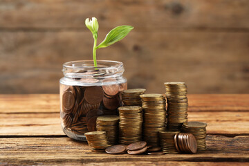 Glass jar with coins and flower on wooden table. Investment concept