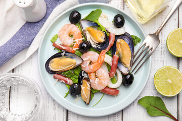 Plate of delicious salad with seafood on white wooden table, flat lay