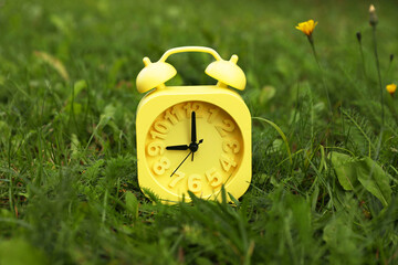 Yellow alarm clock on green grass outdoors