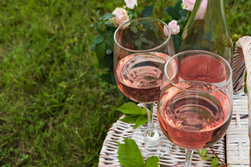 Glasses and bottle of delicious rose wine on picnic basket outdoors, closeup. Space for text