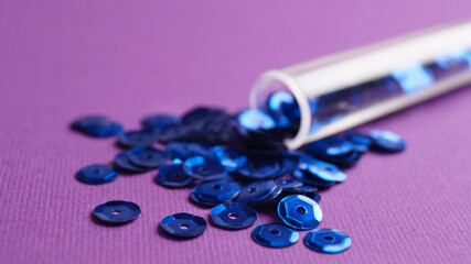 Tube with many blue sequins on purple background, closeup