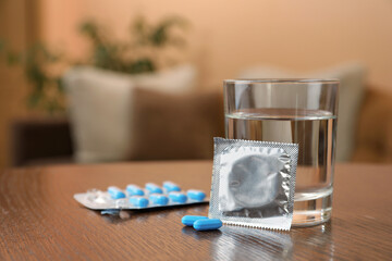 Glass of water, condom and pills on wooden table indoors, space for text. Potency problem concept