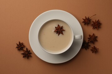 Cup of tea with milk and anise stars on brown background, flat lay