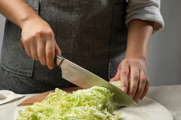 Woman cutting fresh Chinese cabbage at light grey table, closeup