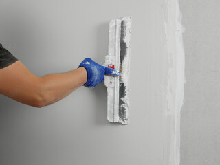 Professional worker plastering wall with putty knife, closeup