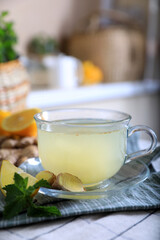 Glass of aromatic ginger tea and ingredients on white checkered tablecloth indoors