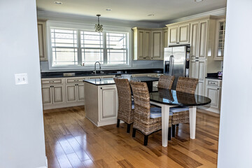 A cream colored new construction kitchen with black granite countertops and wood flooring and stainless steel appliances