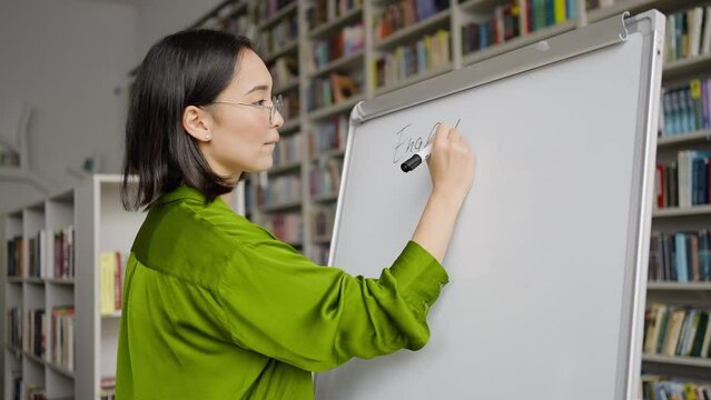 Smiling Asian teacher prepares for lesson writing down topic