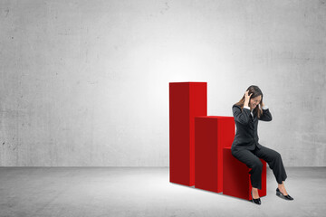 Obraz premium Asian businesswoman sitting on decreasing graph with frustrated expression