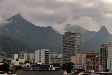 The cloud-shrouded Andaraí Maior and Perdido peaks and the Atlantic rainforest of Tijuca National Park towering above neighboring districts of the Zona Norte, or North Zone of Rio de Janeiro, Brazil - obrazy, fototapety, plakaty