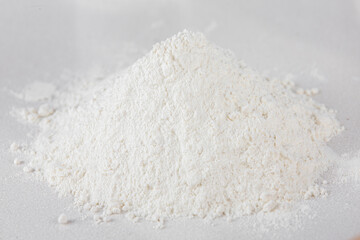 A handful of sifted white flour on a white tabletop background. Scattered flour.