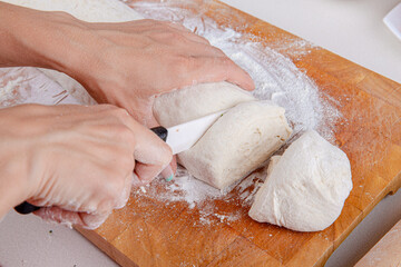 Female hands cut with a knife a kneaded dough on a wooden board. Natural home cooking 