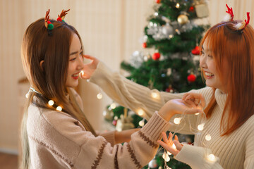 Christmas concept, Two women wears reindeer horns and playing with christmas lights near xmas tree