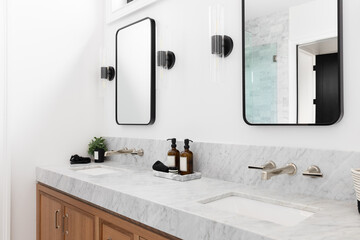 A cozy bathroom with a wood cabinet, marble countertop, and sconces around square mirrors.	 - obrazy, fototapety, plakaty