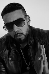 hiphop rapper praying with gold chain on and sun glasses  and ring  on with a leather jacket 