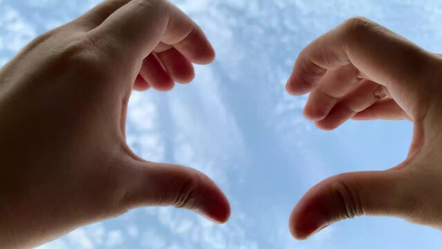 woman's hands forming a heart symbol in the blue sky
