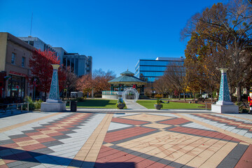 a gorgeous autumn landscape at the Decatur Square with red and yellow autumn trees, lush green trees and a round blue pergola, glass office buildings and clear blue sky in Decatur Georgia USA - obrazy, fototapety, plakaty